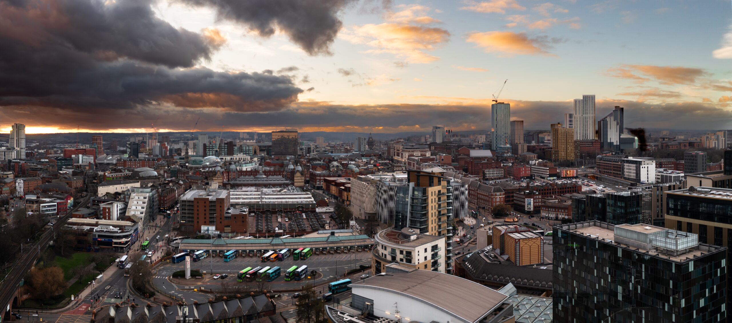 Aerial panoramic view of Leeds city skyline showing a mix of Victorian-era brick buildings and modern high-rise developments at dusk